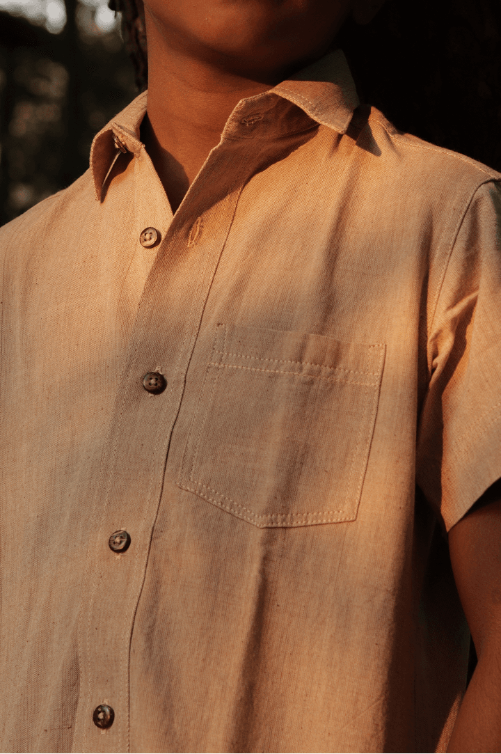 Child wearing a handwoven beige shirt with a front pocket, photographed in warm golden-hour light.
